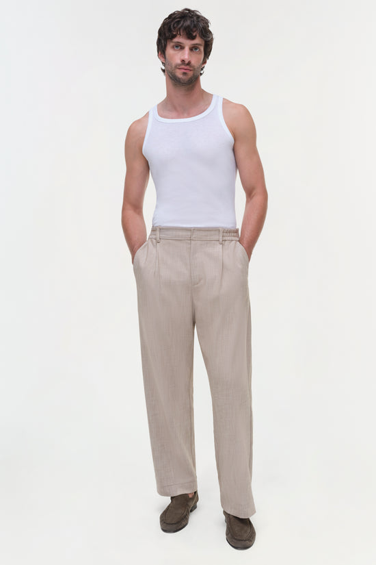 Beige pleated front trousers with side pockets and high waist, styled with white tank top.