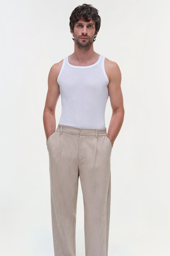 Beige textured pants with flat front and side pockets, styled with white tank top.