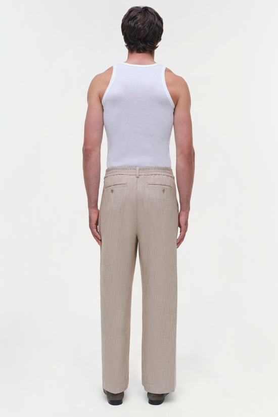 Beige textured pants with flat front and button closure, shown from back view on model wearing white tank top.