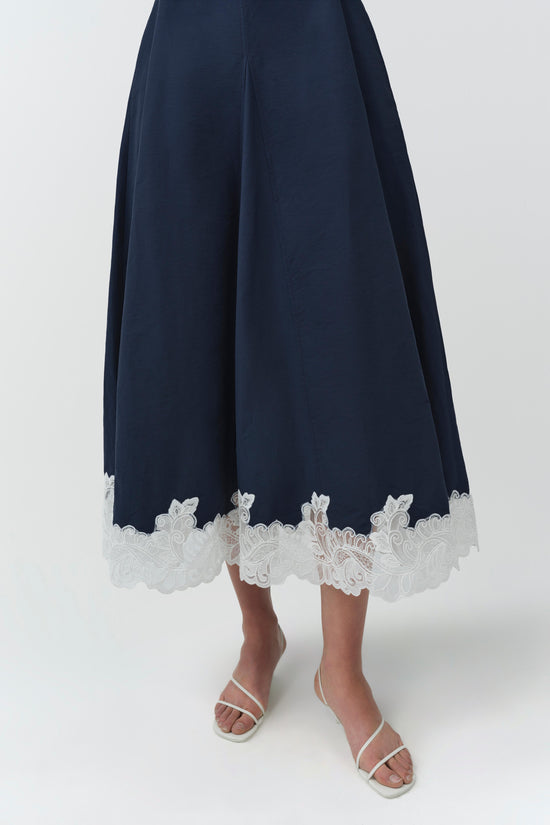 Navy midi dress with white lace trim at hem, worn with white strappy sandals.