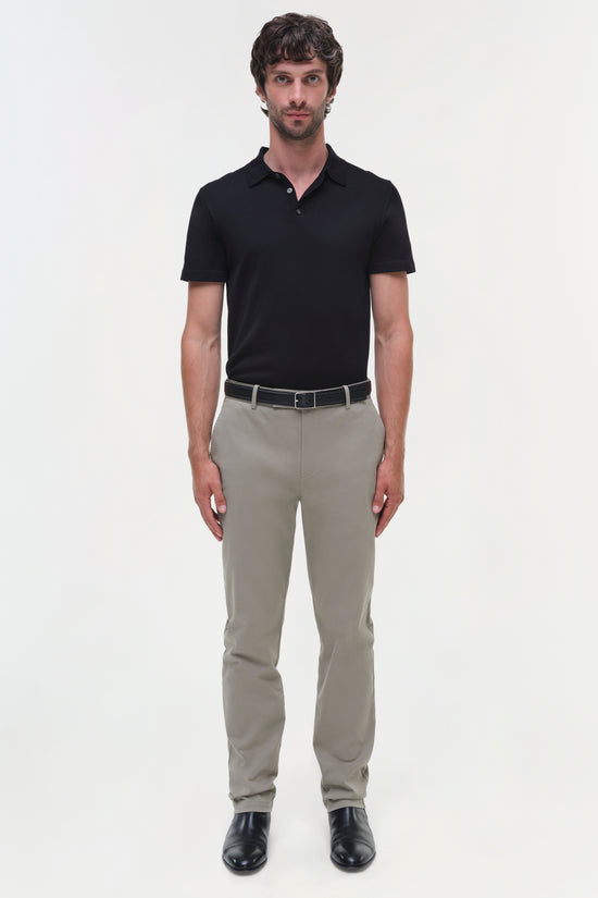 Man wearing black polo shirt and beige cotton twill trousers with belt and black shoes.