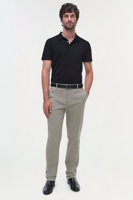 Man wearing beige cotton twill trousers with black polo shirt and dark leather shoes.