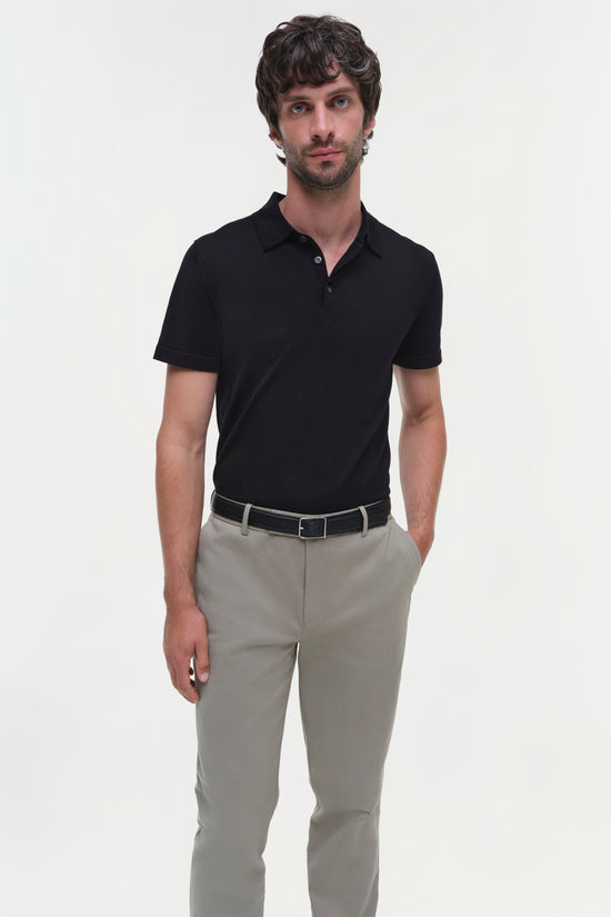 Man wearing beige cotton twill trousers with black polo shirt and belt.