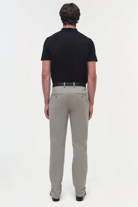 Man wearing black polo shirt and beige cotton twill trousers with belt, shown from back view.