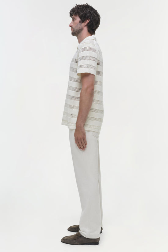 Man wearing cream striped mesh polo shirt with short sleeves and white pants, shown from the side.