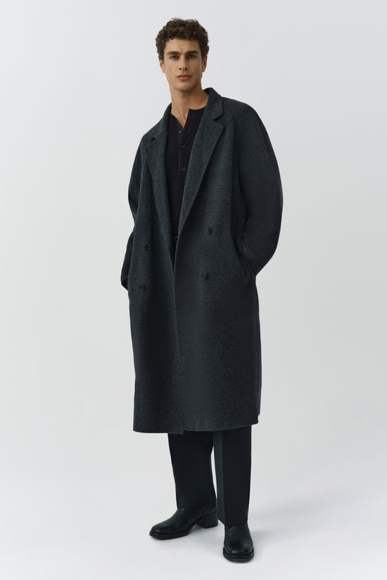 Man wearing charcoal double-breasted wool coat with notch lapels over black shirt and trousers.