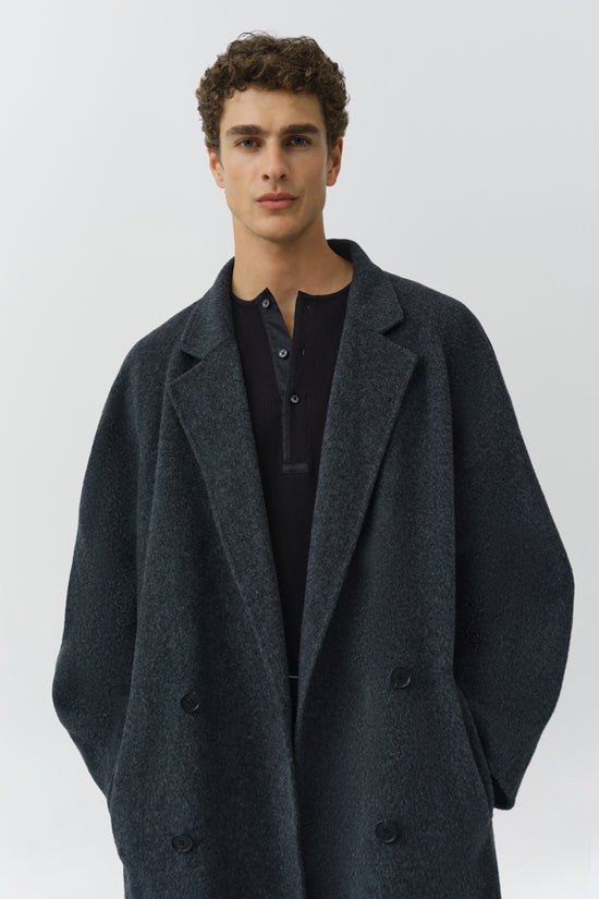 Man wearing charcoal wool double-breasted coat with notched lapels over black ribbed shirt.
