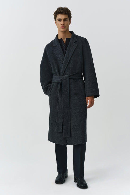 Charcoal gray double-breasted wool coat with notch lapels and tie belt, worn with black trousers and shoes.