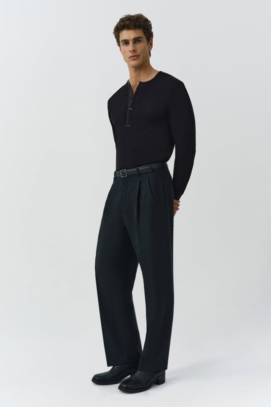 Man wearing black ribbed long-sleeve henley with button placket and dark trousers with belt.