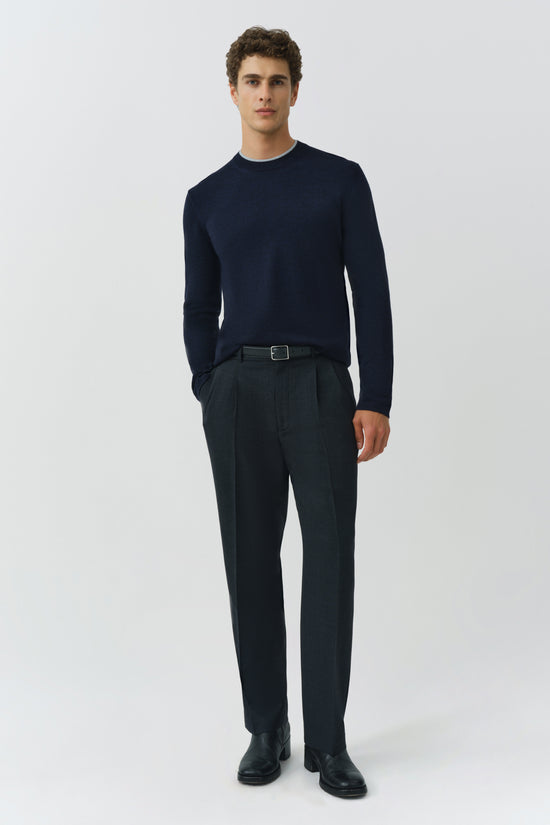 Man wearing navy crewneck sweater with charcoal pleated trousers and black belt.