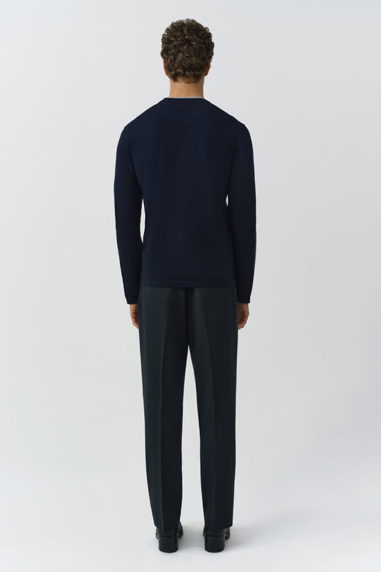Man wearing navy crewneck with long sleeves and dark trousers, shown from back view.