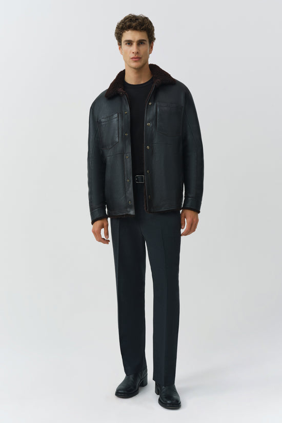 Man wearing black leather shirt jacket with fleece collar and matching black pants.