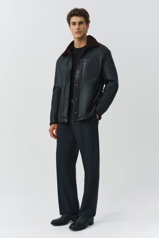 Man wearing dark denim shirt jacket with sherpa collar and button front, styled with black t-shirt and navy pants.