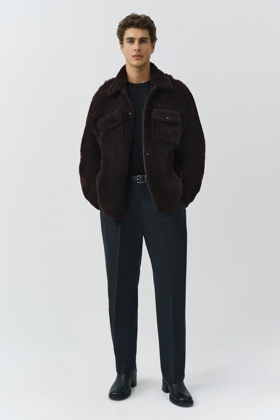 Man wearing dark brown textured shirt jacket with chest pockets and belt, paired with navy trousers and black shoes.