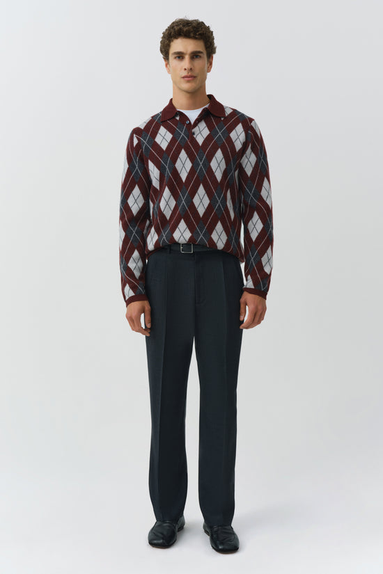Man wearing burgundy and cream argyle polo shirt with collar and navy trousers.