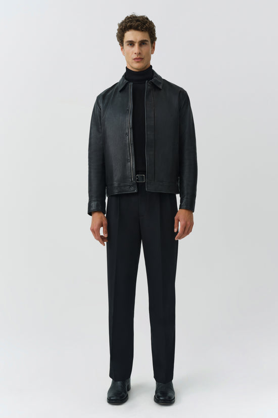 Man wearing black leather jacket with button front and collar over black turtleneck and pants.