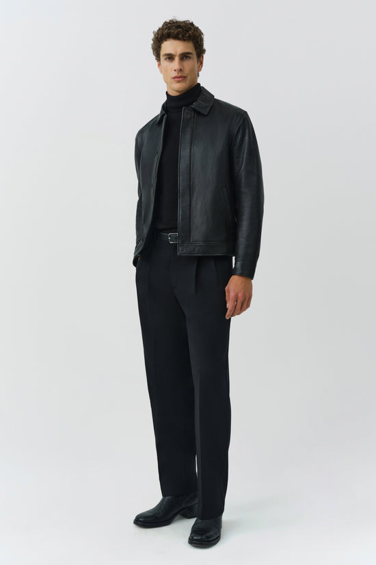 Black leather jacket with collar and belt detail worn over black turtleneck and trousers.