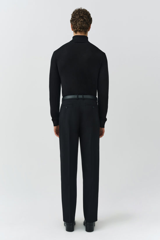 Man wearing black turtleneck and black trousers with belt, shown from back view.