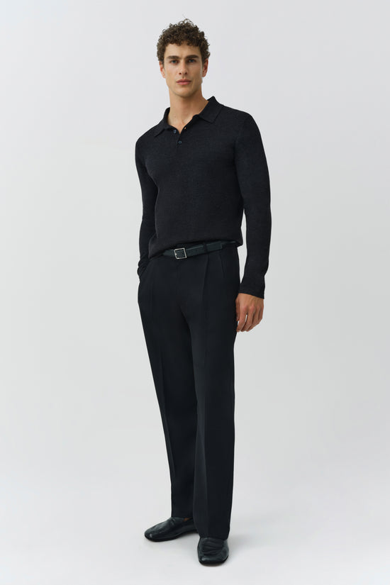 Man wearing black knit polo with long sleeves and collar, paired with black trousers and a dark belt.