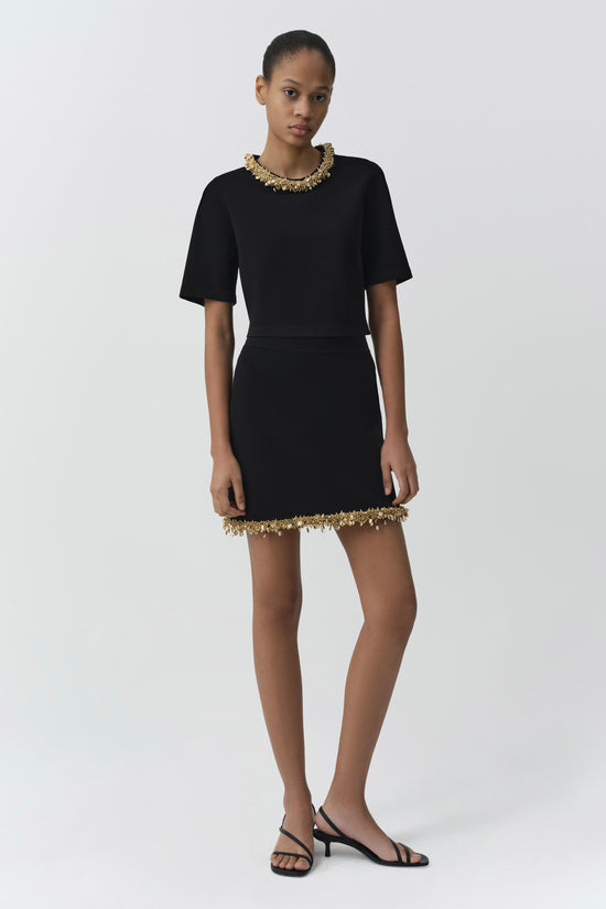 Black knit mini skirt with gold beaded trim at neckline and hem, paired with matching short-sleeve top.