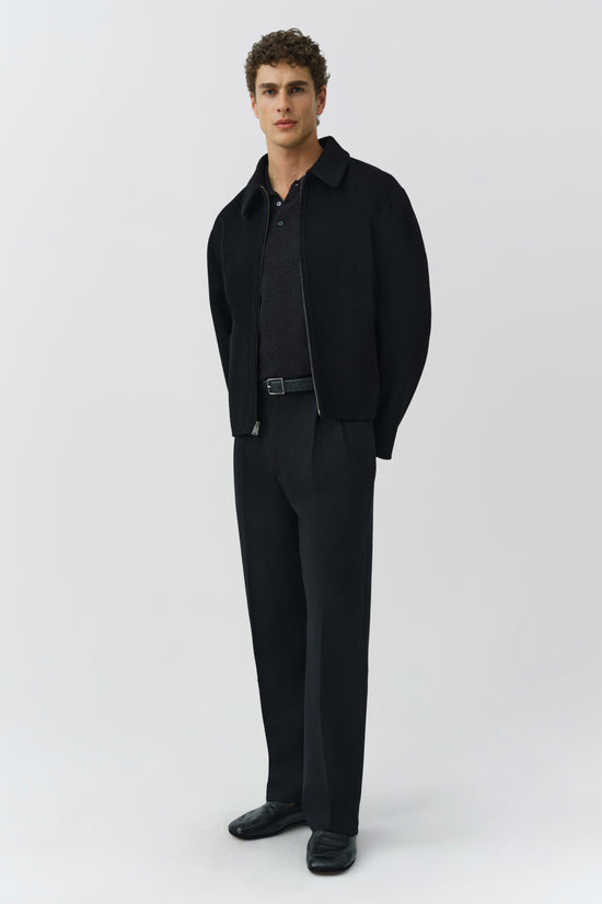 Man wearing black Quinn Jacket with collar, zipped over charcoal polo shirt, paired with black trousers and black shoes.