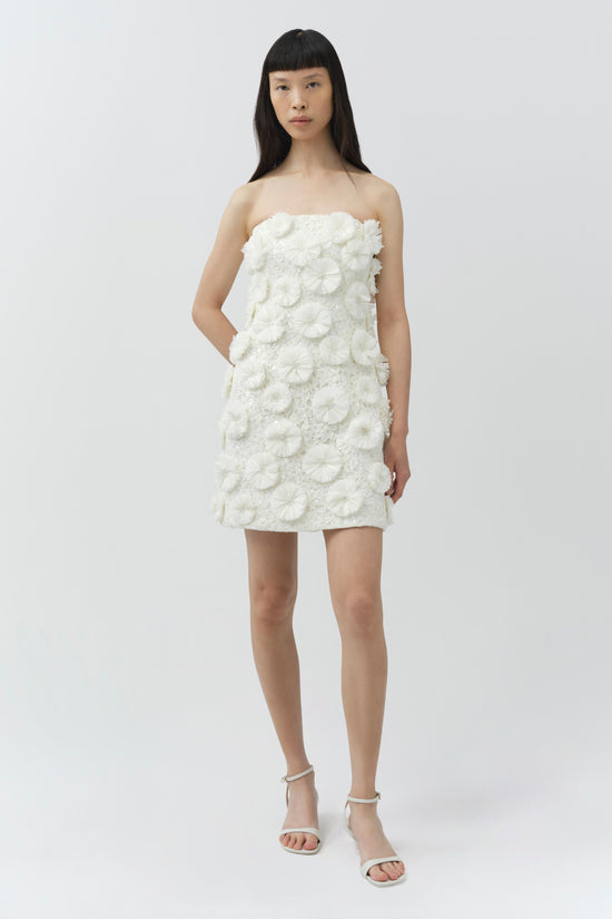 Cream strapless mini dress with textured floral raffia embellishments throughout, worn with white ankle-strap sandals.