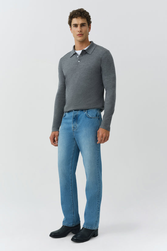 Man wearing gray knit polo shirt with collar and button placket, paired with blue denim jeans and black boots.