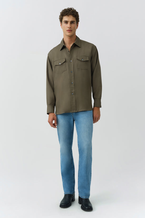 Olive-green workwear shirt with chest pockets and button front, worn with blue jeans and black boots.