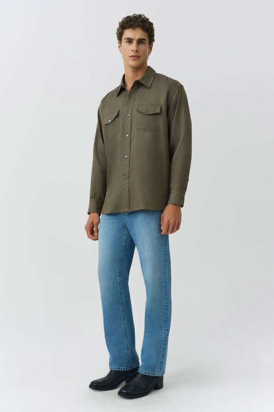 Man wearing olive-green button-up shirt with chest pockets, blue jeans, and black boots.