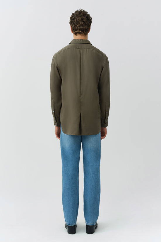 Man wearing olive green long-sleeve button-up shirt with blue jeans, shown from back view.