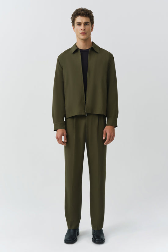Olive green jacket with collar and zip front worn over black t-shirt, paired with matching olive trousers.