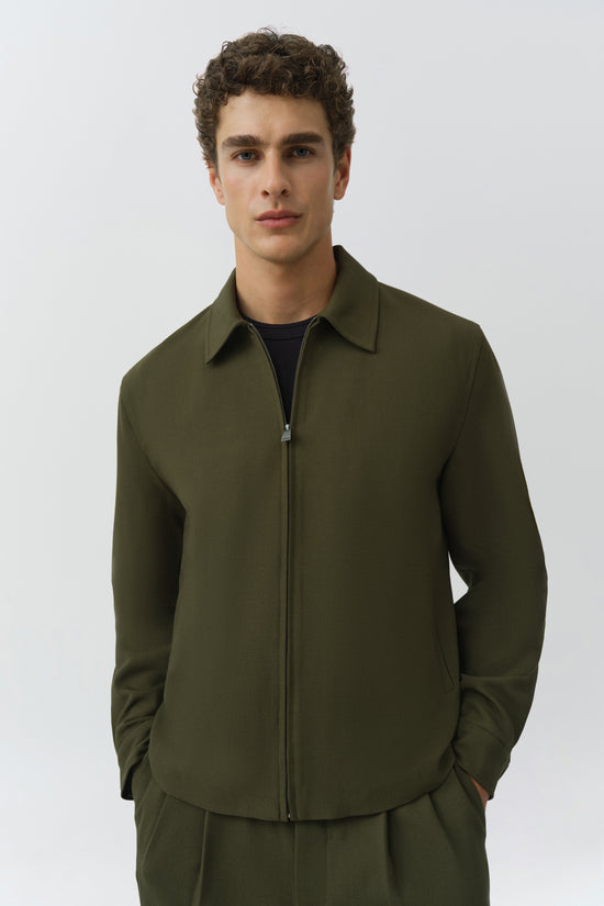 Olive green jacket with spread collar and full-length zipper, worn over black shirt.