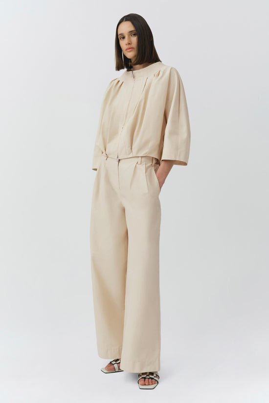 Cream cotton jacket with pleated front and three-quarter sleeves, paired with matching high-waisted trousers.