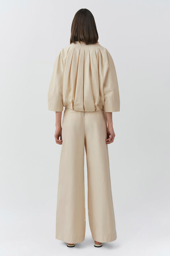Cream pleated cotton jacket with three-quarter sleeves shown from back, paired with matching wide-leg trousers.