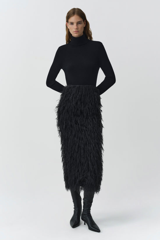 Black fringe midi skirt with textured jacquard pattern, styled with black turtleneck and boots.