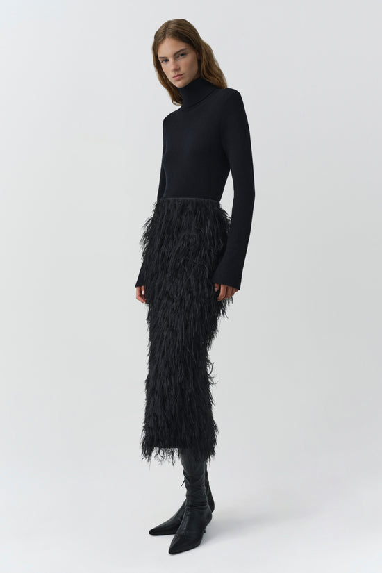 Black midi skirt with fringe texture worn with black turtleneck and black boots.
