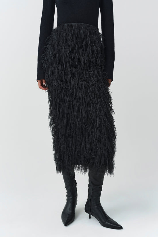 Black midi skirt with layered fringe texture worn with black long-sleeve top and black boots.
