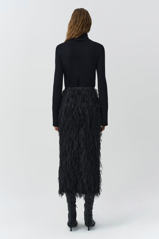 Black midi skirt with fringe texture throughout, worn with black long-sleeve top and boots, rear view.
