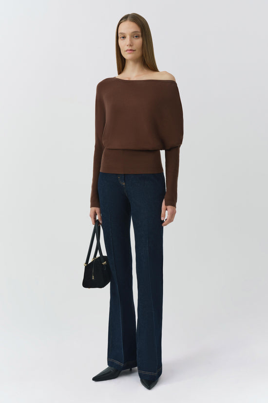 Brown off-shoulder cropped sweater with ribbed waistband worn with dark blue jeans.