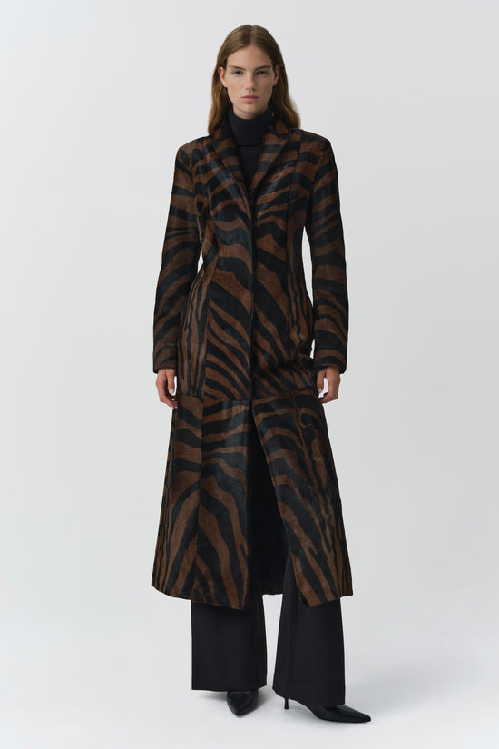 Brown and black zebra-striped calf hair coat with notch lapels, worn open over black turtleneck and pants.