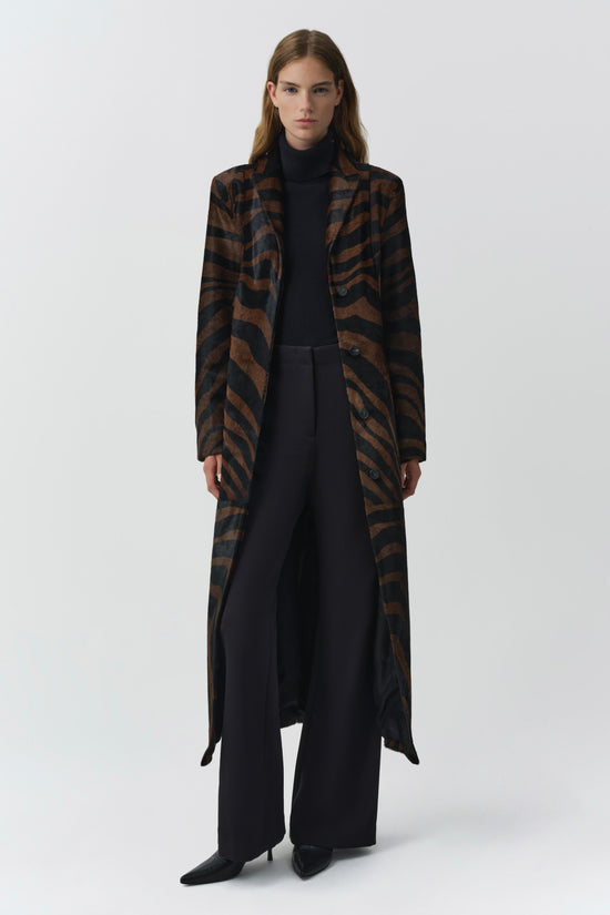 Brown and black zebra-striped long coat with notched lapels worn over black turtleneck and pants.