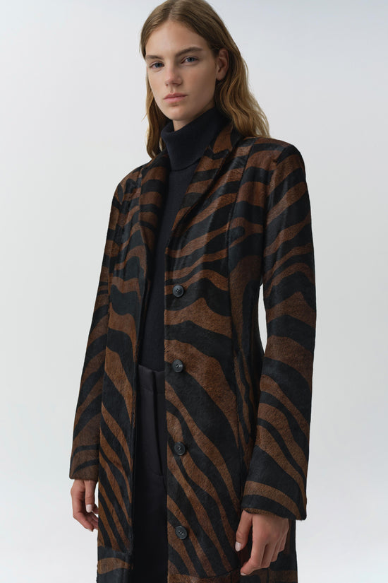 Brown and black zebra-striped calf hair coat with button front and notch collar worn over black turtleneck.