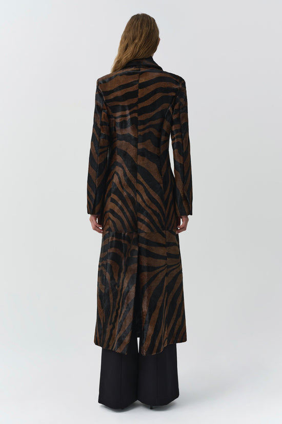 Brown and black zebra-striped calf hair coat with long sleeves and flowing silhouette, worn over black pants.