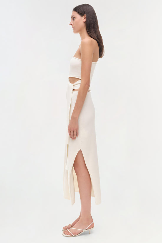 Cream strapless midi dress with cutout details at the side, shown on model in profile view.