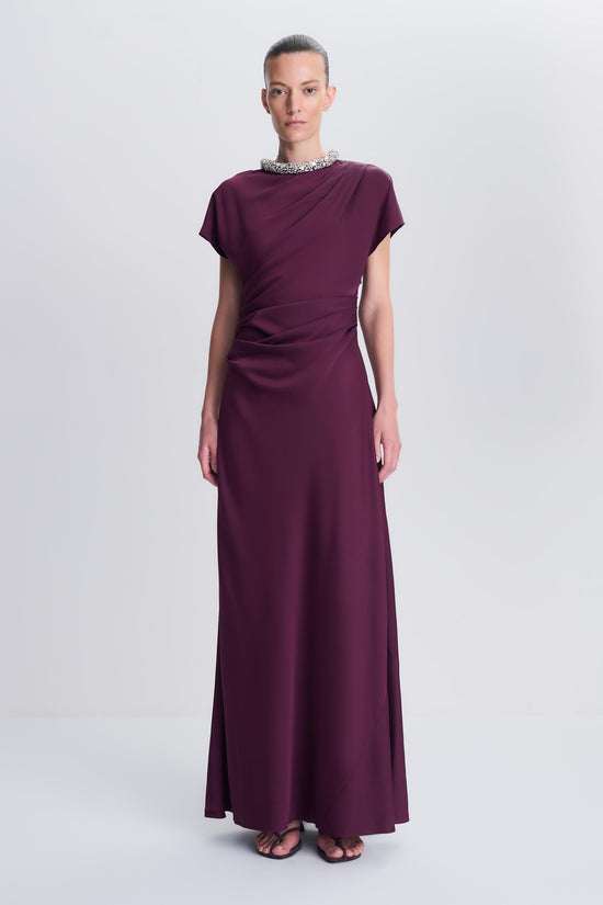 Woman wearing plum satin gown with beaded neckline, short sleeves, and floor-length skirt.
