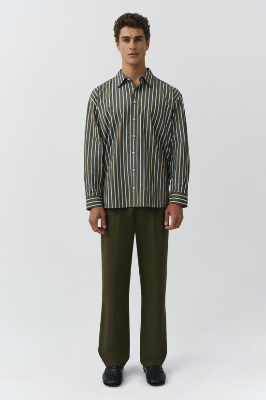 Oversized button-up shirt with vertical stripes in charcoal and cream, worn with olive green trousers.