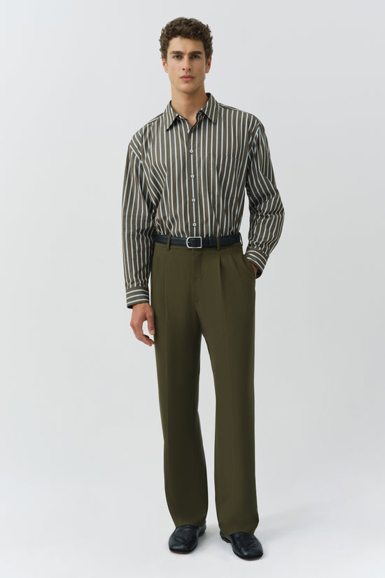 Man wearing olive and cream striped oversized button-up shirt with olive trousers and black belt.