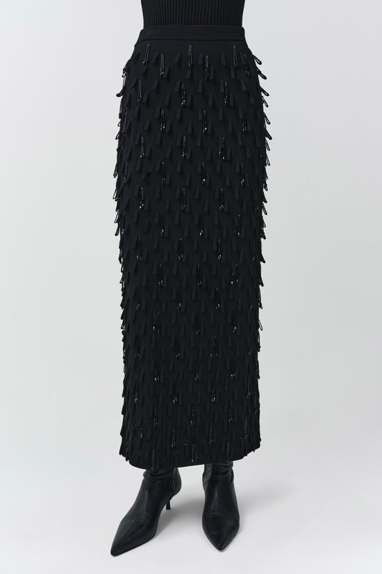 Black knit midi skirt with fringe and bead embellishments throughout, paired with black pointed-toe boots.
