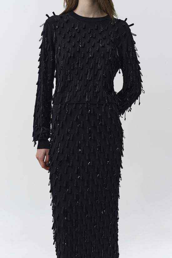Black knit midi skirt with beaded fringe embellishments throughout, styled with matching long-sleeve top.