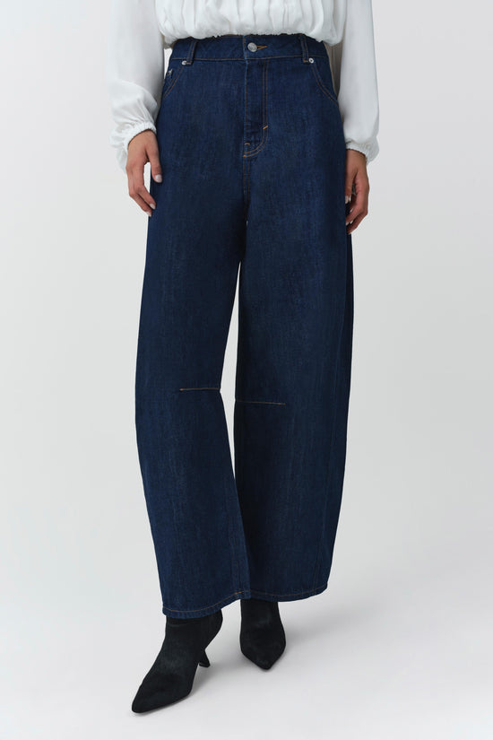 Dark blue wide-leg jeans with ripped knee panels, worn with white blouse and black ankle boots.